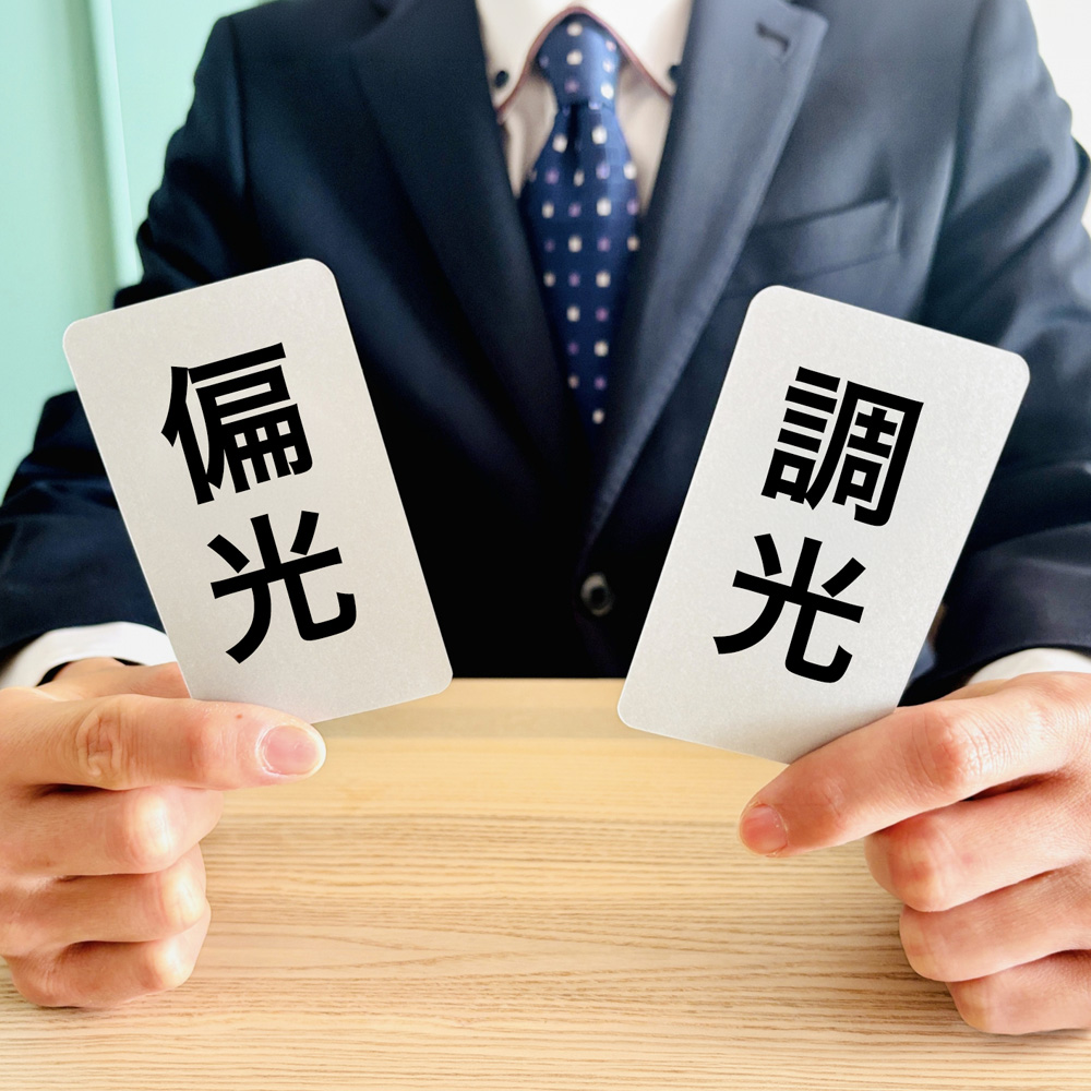 「偏光」と「調光」と書かれた2枚のカードを手に持ち、どちらの機能が必要か選択を迫るビジネスマンのイメージ