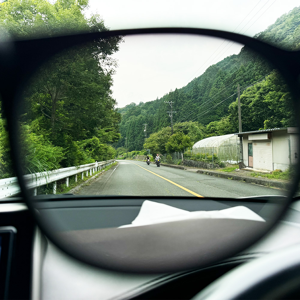 偏光レンズ越しの運転席からの視界。ダッシュボードの映り込みが消え、緑の木々や路面のセンターラインが鮮明に見えている、夏のドライブを快適にするアイキャッチ画像。